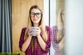 Young freelance lady drinking coffee in casual clothes and looking through a window. Morning. Royalty Free Stock Photo