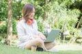 Young freelancer with headphones using laptop in a green park. Cheerful modern woman sitting outdoors in park on a grass and using Royalty Free Stock Photo
