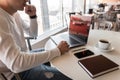 Young freelancer man is resting sitting at a table in a cafe with a modern laptop with a cup of coffee with a smartphone Royalty Free Stock Photo