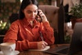 Young freelancer woman taking notes in a notepad, calling on the phone while working on a computer in a cafe. Royalty Free Stock Photo