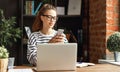 Young freelancer works on a laptop and searches for information in your smartphone in her home office