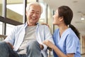 Young friendly asian female caregiver talking to elderly man in nursing home