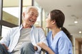 Young friendly asian female caregiver talking to elderly man in nursing home