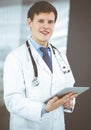 Young friendly doctor is checking some information on his computer tablet. Portrait of a professional physician at work