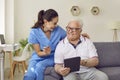 Young friendly female caregiver and senior man using digital tablet together in nursing home. Royalty Free Stock Photo