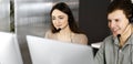 Young friendly man in headsets is talking to the client, while sitting at the desk with a female colleague in an office Royalty Free Stock Photo