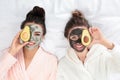Young friends with facial masks  fun on bed at pamper party, top view Royalty Free Stock Photo