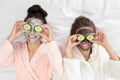 Young friends with facial masks having funon bed at pamper party, top view