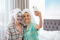 Friends with facial masks taking selfie in bedroom at pamper party