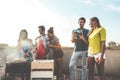 Young friends having barbecue party at sunset on terrace - Happy people doing bbq dinner outdoor cooking meat and drinking wine -