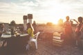 Young friends having barbecue party at sunset on terrace patio - Happy people doing bbq dinner outdoor cooking meat and drinking