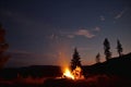 Young friends near bright bonfire in camp at night getting warm sitting near fire Royalty Free Stock Photo