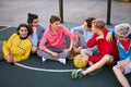 Young friends sitting on basketball court, relaxing and taking break after game