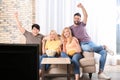 Young friends with snacks watching TV on sofa