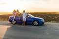 Young three friends standing near convertible car and talking each other have fun on beauty sunset on the road Royalty Free Stock Photo