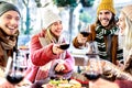 Young friends toasting red wine at restaurant patio - Happy people having fun together at winery bar wearing winter clothes - Royalty Free Stock Photo