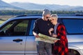 Happy tourist couple with paper map near rented car. Trendy young people using map. Traveling by car on summer vacations Royalty Free Stock Photo