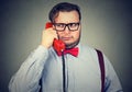 Frowning man having problem while speaking on red telephone feeling confused and suspicious on gray background