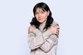 Young frozen woman in sweater with clasped hands gesturing coldly, on light studio background