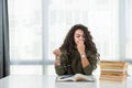 Young frustrated school girl sitting at desk with pile of books feeling sad that she need to read. Female first year college