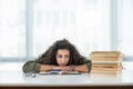 Young frustrated school girl sitting at desk with pile of books feeling sad that she need to read. Female first year college