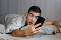 Young frustrated and stressed man is late. He is waking up, looking at smartphone and is shocked. The concept of a modern rhythm o Royalty Free Stock Photo