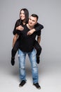 Young fun couple having fun riding piggy back laughing on grey background Royalty Free Stock Photo