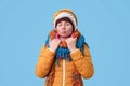 Young funny adult woman in hat and winter scarf waiting kiss with closed eyes on blue wall