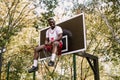 Young funny African American basketball player in a white T-shirt and red shorts sits in a basket on the basketball