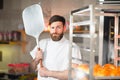 A young funny baker with a pizza spatula in his hands against the backdrop of an oven.