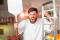 A young funny baker with a pizza spatula in his hands against the backdrop of an oven.