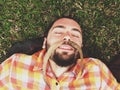 Young Funny Bearded Hipster Man Laying on the Ground with Mustache Made of Autumn Long Leaves on His face.