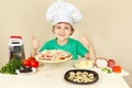 Young funny boy in chefs hat enjoys cooking tasty pizza Royalty Free Stock Photo