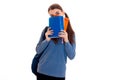 Young funny brunette student girl with backpack on her shoulders hiding her face behind a books isolated on white Royalty Free Stock Photo