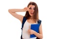 Young funny brunette student woman with blue backpack on her shoulder and folder for notebooks in hands looking at the Royalty Free Stock Photo