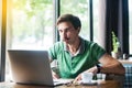 Young funny businessman in green t-shirt sitting and looking at laptop display with stupid crazy face and crossed eyes