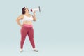 Young funny fat woman in sportswear screaming with mouthpiece on studio blue background. Royalty Free Stock Photo