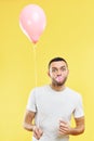 Young funny man blowing chewing gum bubble and holding pink air balloon