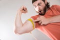 Young funny man measuring biceps, muscles of his arm with a yellow tape measure Royalty Free Stock Photo