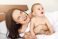 Young funny mom playing the ape her baby crying lying in bed at home. Royalty Free Stock Photo