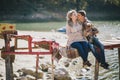Young future parents and their dog in a funny costume sitting on a wooden bridge and having picnic near lake Royalty Free Stock Photo