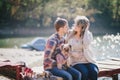 Young future parents and their dog in a funny costume sitting on a wooden bridge and having picnic near lake Royalty Free Stock Photo