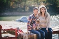 Young future parents and their dog in a funny costume sitting on a wooden bridge and having picnic near lake Royalty Free Stock Photo