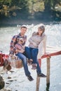 Young future parents and their dog in a funny costume sitting on a wooden bridge and having picnic near lake Royalty Free Stock Photo