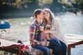 Young future parents and their dog in a funny costume sitting on a wooden bridge and having picnic near lake Royalty Free Stock Photo