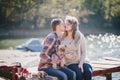 Young future parents and their dog in a funny costume sitting on a wooden bridge and having picnic near lake Royalty Free Stock Photo