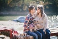 Young future parents and their dog in a funny costume sitting on a wooden bridge and having picnic near lake Royalty Free Stock Photo