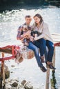 Young future parents and their dog in a funny costume sitting on a wooden bridge and having picnic near lake Royalty Free Stock Photo