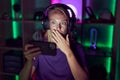 Young gamer woman playing video games with smartphone covering mouth with hand, shocked and afraid for mistake Royalty Free Stock Photo