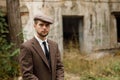 A young gangster with a beard stands on the street near an abandoned building. Retro. Outdoors.